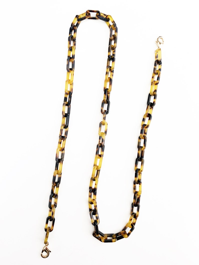 May include: A long, brown and yellow chain with a tortoiseshell pattern. The chain has two gold clasps at the ends.