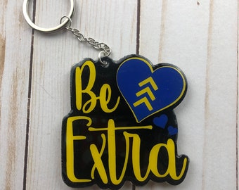 May include: A black and yellow key chain with the text "Be Extra" and a blue heart with a white chevron design.