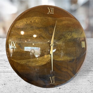 May include: A round, brown clock with gold Roman numeral markings and gold hands. The clock face has a marbled, glittery appearance.