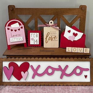 May include: A wooden Valentine's Day decor set with a mailbox, a sign that says "Love Letters", a sign that says "Feb 14", a sign that says "Love", a red envelope with a pink heart, and a sign that says "Love" with wooden letter blocks. There is also a sign that says "XOXO" with two pink hearts and a sign that says "Sending Love To You - Hugs & Kisses - XOXO" with a red lip print.