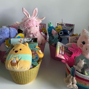 Könnte beinhalten: Mehrere Osterkörbe gefüllt mit Plüschtieren und Leckereien. Die Körbe enthalten Stofftiere wie einen Esel, Winnie Puuh, ein Einhorn und ein Kaninchen. Weitere Artikel sind Malbücher, Süßigkeiten und kleine Spielzeuge. Die Körbe sind in verschiedenen Farben und Stilen.