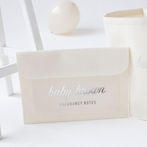 Può includere: Una busta bianca con una scritta in lamina argentata che recita "baby brown pregnancy notes".