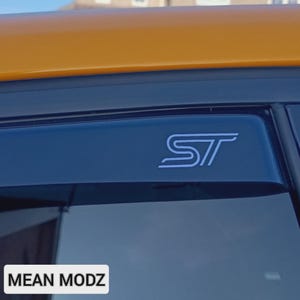 May include: A dark blue car window visor featuring a white "ST" logo. The visor is attached to a vehicle with an orange roof. The text "MEAN MODZ" is visible at the bottom of the image.
