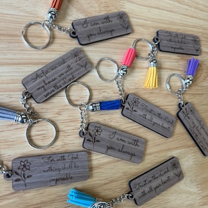May include: A set of 10 wooden keychains with inspirational quotes and tassels. The keychains feature different colors of tassels, including blue, yellow, orange, and purple. The quotes include "I am with you always", "Trust in the Lord with all your heart", and "For with God nothing shall be impossible".