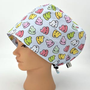 May include: A light blue surgical scrub cap featuring a repeating pattern of colorful, smiling poop emojis. The cap has a drawstring for adjustment and a small tag that says "gray".