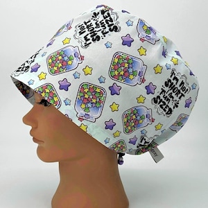 May include: A light blue surgical scrub cap with a repeating pattern of jars filled with colorful star-shaped confetti and stars. The cap has the text "I'm Not Short, I'm Fun Sized" in black. A small tag is attached to the cap.