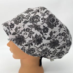 May include: A white scrub cap with a black floral pattern. The cap has a tie at the back.