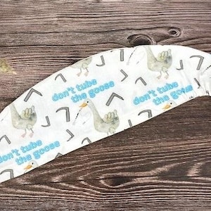 May include: White fabric headband with a repeating pattern of geese and the text "don't tube the goose".