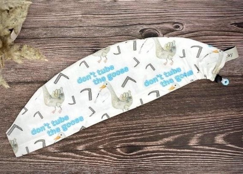 May include: White fabric headband with a repeating pattern of geese and the text "don't tube the goose".