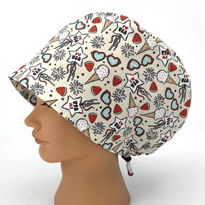 May include: A scrub cap with a cream background featuring a repeating pattern of red, white, and blue icons including ice cream cones, watermelon slices, heart-shaped sunglasses, fireworks, and stars with the text I LOVE USA printed inside.