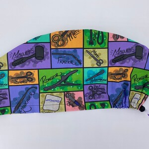 May include: A colorful surgical scrub hat with a pattern of various medical instruments and their names, including "Mallet", "Rake", "Mayo", "Frazier", "Rongeur", "Snap", "Yankauer", and "Hohmann".