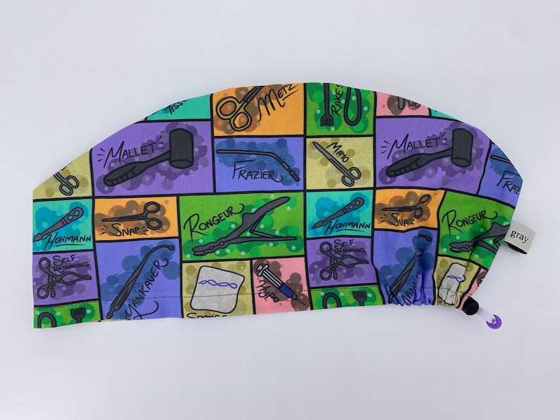 May include: A colorful surgical scrub hat with a pattern of various medical instruments and their names, including "Mallet", "Rake", "Mayo", "Frazier", "Rongeur", "Snap", "Yankauer", and "Hohmann".