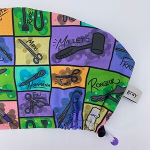 May include: A colorful surgical cap with a variety of medical instruments and tools printed on it. The cap is made of a soft, stretchy fabric and has a drawstring closure. The cap is labeled "gray".