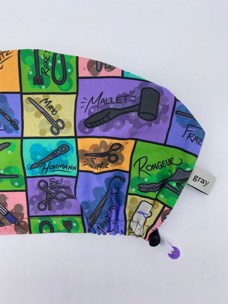 May include: A colorful surgical cap with a variety of medical instruments and tools printed on it. The cap is made of a soft, stretchy fabric and has a drawstring closure. The cap is labeled "gray".
