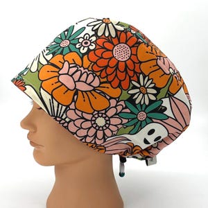 May include: A colorful floral patterned scrub cap featuring orange, pink, green, and white flowers. The cap has a drawstring and is designed to be worn in a medical or professional setting. The cap is made of a soft, lightweight fabric.