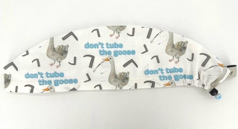May include: White surgical scrub hat with a repeating pattern of geese and the text "don't tube the goose".