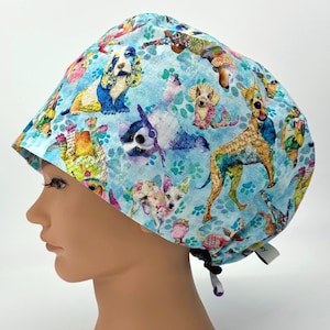 May include: A blue scrub hat with a colorful print of dogs and paw prints. The hat has a tie at the back.