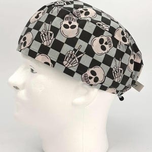 May include: A black and gray checkered scrub hat with a skull and crossbones pattern. The hat has a tie at the back.
