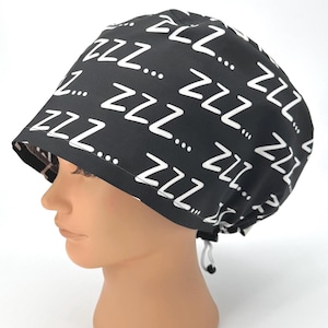 May include: A black surgical scrub cap with a white "zzz" pattern. The cap has a tie in the back for adjustment. The fabric is printed with the word "zzz" and three dots in a repeating pattern.