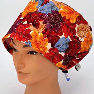 May include: A white scrub hat with a colorful fall leaf print. The hat has a tie at the back and a small tag that says "Bray".