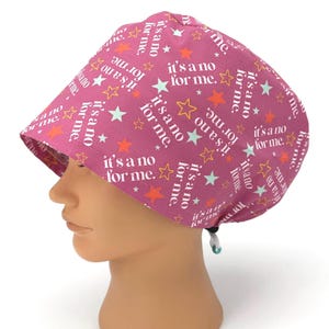 May include: A magenta surgical scrub cap with a repeating pattern of white text that reads "it's a no for me" and colorful stars. The cap has a curved brim and an adjustable drawstring at the back.
