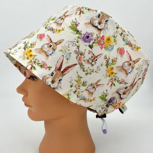 May include: A white scrub hat with a floral pattern featuring bunnies and flowers. The hat has a drawstring closure.