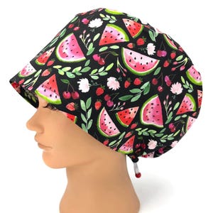 May include: A black scrub cap featuring a vibrant pattern of watermelon slices, cherries, strawberries, and white flowers. Green leaves and stems are interspersed throughout the design. The cap has a drawstring for an adjustable fit.