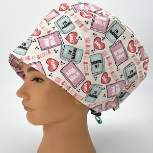 May include: A white scrub hat with a pink and green print of books and hearts. The text on the books says "The book is better" and "I'm reading".