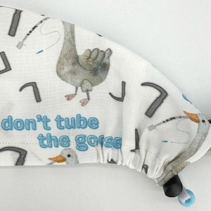May include: White scrub hat with a blue and gray goose print and the text "don't tube the goose".
