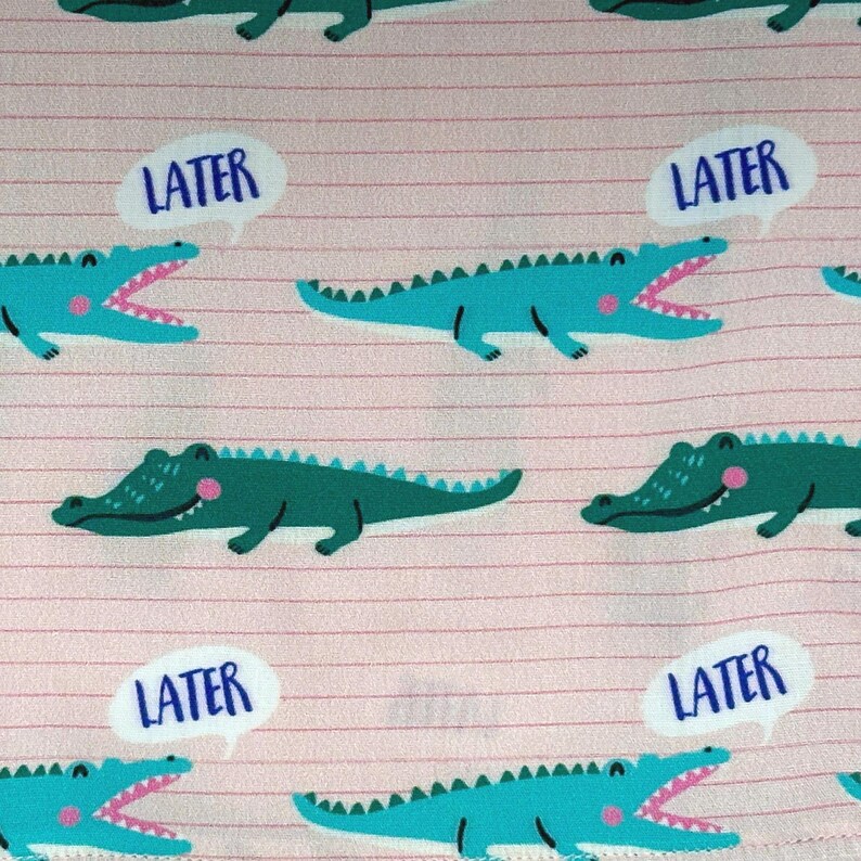 May include: Pink fabric with a repeating pattern of cartoon alligators in teal and green. Each alligator has an open mouth and a pink tongue. White speech bubbles with the word "LATER" are scattered throughout the design.