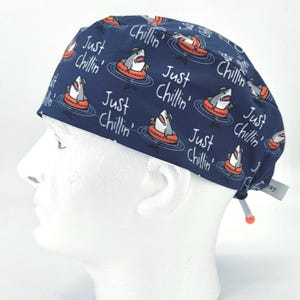 May include: Blue surgical scrub hat with a repeating pattern of white sharks wearing sunglasses and life preservers. The text "Just Chillin'" is repeated throughout the pattern.
