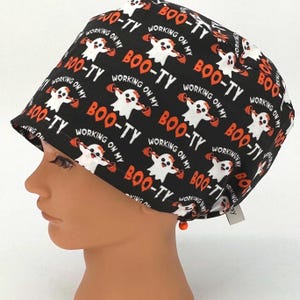 May include: Black scrub hat with a white ghost and orange text that reads "Working on my Boo-ty".