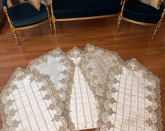 May include: Three white prayer rugs with gold lace trim and a quilted design. The rugs are arranged in a fan shape on a wooden floor.