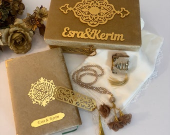 May include: A gold velvet box with an intricate design and the names "Esra & Kerim" inscribed on the front. The box contains a gold-colored book, a set of prayer beads, a small gold-colored box, and a white fabric with lace trim.