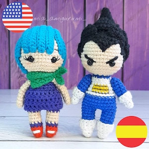 Può includere: Due figure amigurumi all'uncinetto, una blu con capelli blu e una sciarpa verde, l'altra nera con capelli neri, che indossa un abito blu e giallo. Le figure sono in piedi su una superficie di legno. Il testo "mia_amigurumi_" è visibile sullo sfondo.