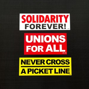 Könnte beinhalten: Drei rote und gelbe Aufkleber mit weißem Text. Der obere Aufkleber lautet "Solidarität für immer!" Der mittlere Aufkleber lautet "Gewerkschaften für alle". Der untere Aufkleber lautet "Niemals eine Streikpostenlinie überqueren".