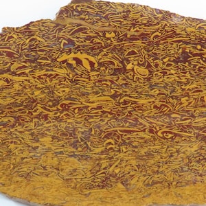 May include: A natural stone slab with a unique pattern. The surface is a mix of deep red and golden yellow, creating a striking contrast. The intricate design resembles a network of lines and shapes.