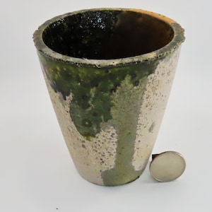 May include: A ceramic planter with a green, white, and brown glaze. The planter is cone-shaped and has a rough, textured surface.
