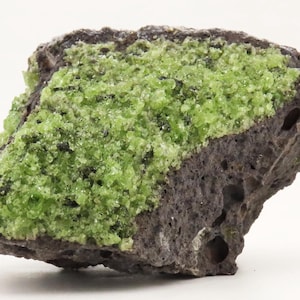 May include: A rough, dark gray rock with a vibrant, lime green crystalline formation across the top. The rock has a porous texture with small holes and a slightly rounded shape. The green crystals are clustered and uneven.