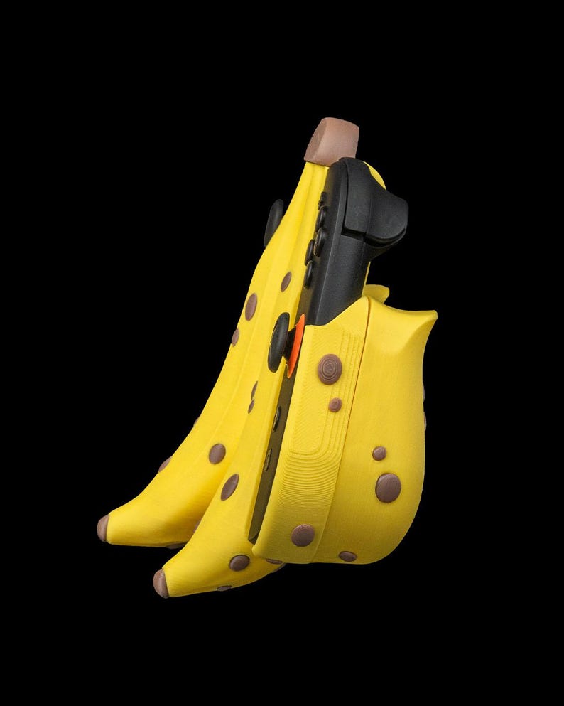 K&ouml;nnte beinhalten: Eine gelbe Bananen-f&ouml;rmige H&uuml;lle mit braunen Flecken, die ein schwarzes elektronisches Ger&auml;t enth&auml;lt. Die H&uuml;lle hat eine braune Spitze und ist vor einem schwarzen Hintergrund platziert. Das Ger&auml;t hat schwarze Kn&ouml;pfe und einen orangefarbenen Akzent.