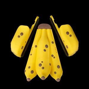 K&ouml;nnte beinhalten: Eine Ansammlung gelber, bananenf&ouml;rmiger Objekte mit braunen Flecken und Spitzen, vor schwarzem Hintergrund. Die Objekte haben ein strukturiertes Aussehen und sind in einer ansprechenden Komposition angeordnet, die ein spielerisches oder k&uuml;nstlerisches Thema suggeriert.