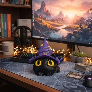 May include: A black cat figurine wearing a purple wizard hat with a gold emblem. The cat has large yellow eyes and is sitting on a patterned desk mat. A computer monitor displays a landscape scene in the background.