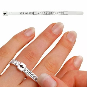 May include: A white ring sizer tool with black markings and the text "SIZE & HALF SIZES". The tool is wrapped around a finger to measure ring size. Numbers from 1 to 17 are visible.