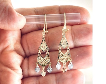 May include: Gold-toned dangle earrings with intricate filigree designs. Each earring features a triangular top, a decorative middle section, and three dangling charms in gold and silver tones. The earrings are held up by a clear plastic stick.