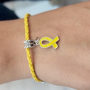 May include: A yellow braided bracelet with a yellow ribbon charm. The ribbon charm is a symbol of support and awareness.