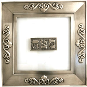 Peut inclure: Une décoration murale encadrée en argent avec un design orné. Le cadre a un devant en verre et une plaque en argent avec le mot hébreu "Shalom" en relief.