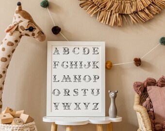 May include: A framed alphabet print in a white frame, displayed on a small wooden table. The letters are in a decorative font. A stuffed giraffe, wooden blocks, and a decorative garland with pom-poms are also in the image.