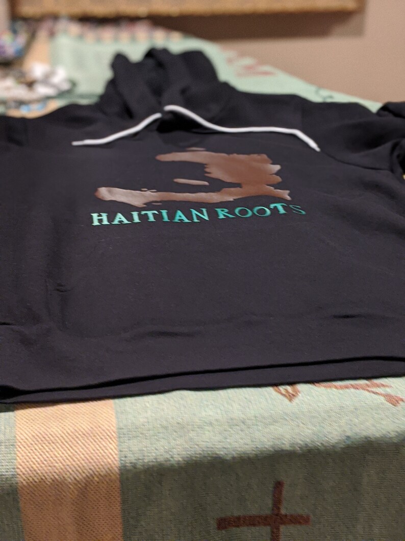 May include: Black hooded sweatshirt with a brown outline of the island of Haiti and the text "HAITIAN ROOTS" in green.