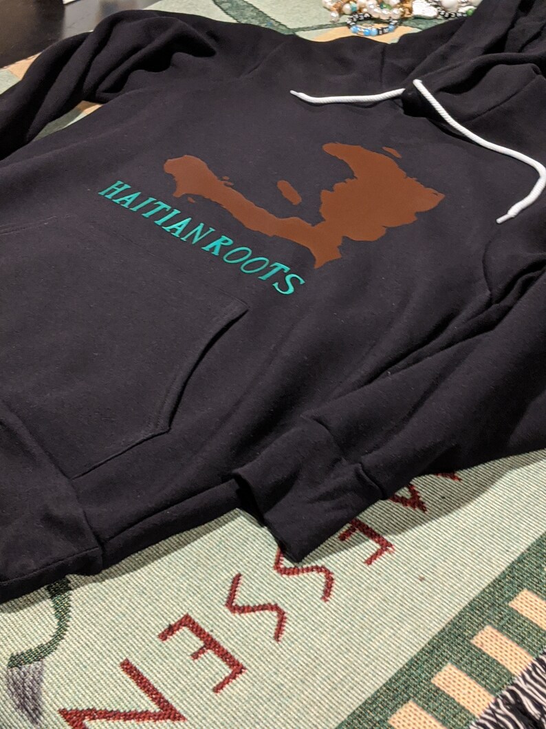 May include: Black hooded sweatshirt with a brown outline of Haiti and the text "Haitian Roots" in teal green.