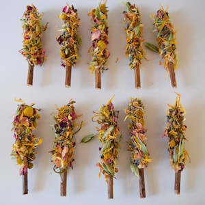 K&ouml;nnte beinhalten: Draufsicht auf zehn R&auml;ucherb&uuml;ndel aus getrockneten Blumen. Die St&auml;be bestehen aus Holzst&auml;ben, die mit getrockneten Blumen und Kr&auml;utern umwickelt sind. Die Blumen sind gelb, orange, rosa und lila. Auf wei&szlig;em Hintergrund angeordnet.